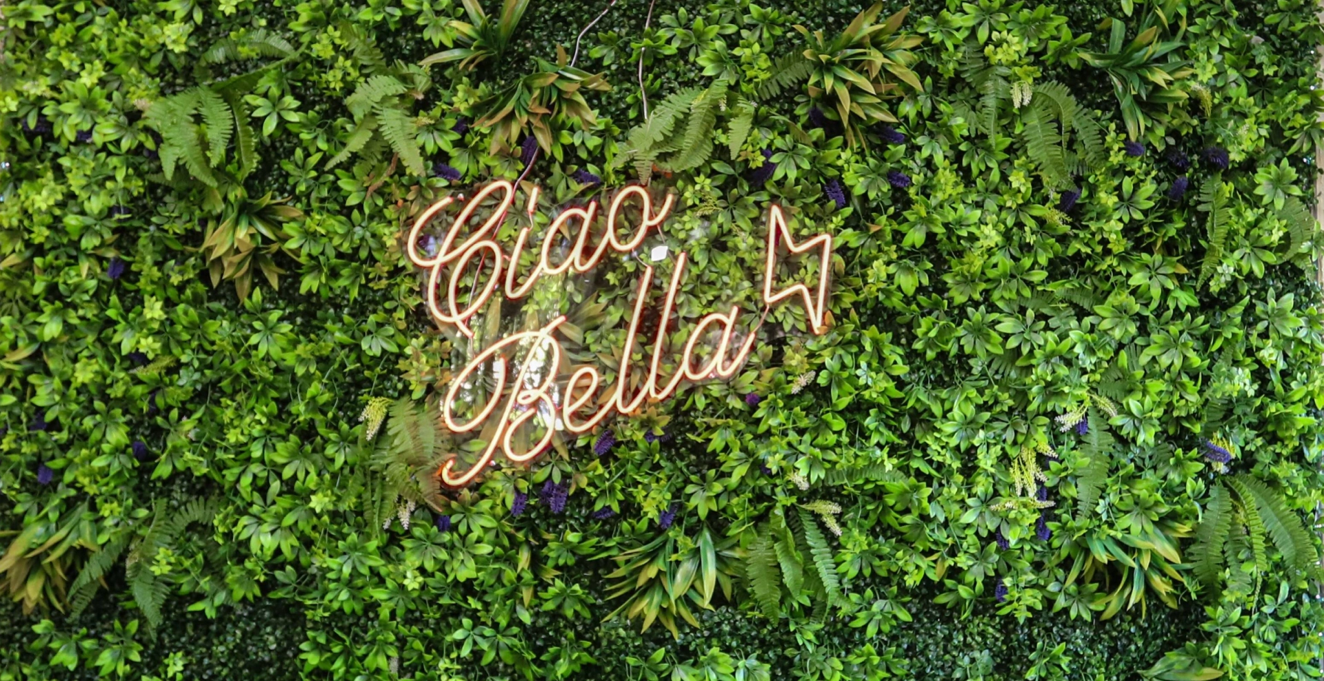 Table with floral décor beneath a glowing Ciao Bella sign.